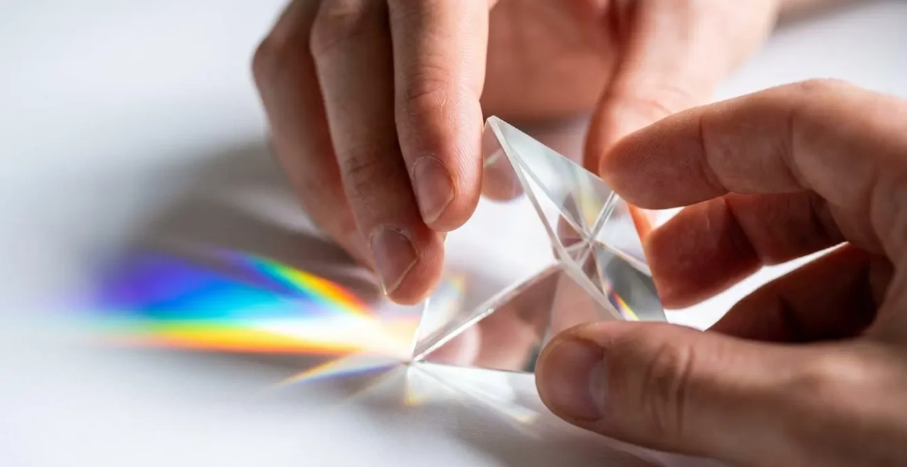 Primer plano de manos sosteniendo un prisma de cristal que refracta la luz en múltiples colores, representando perspectivas diversas del pensamiento lateral